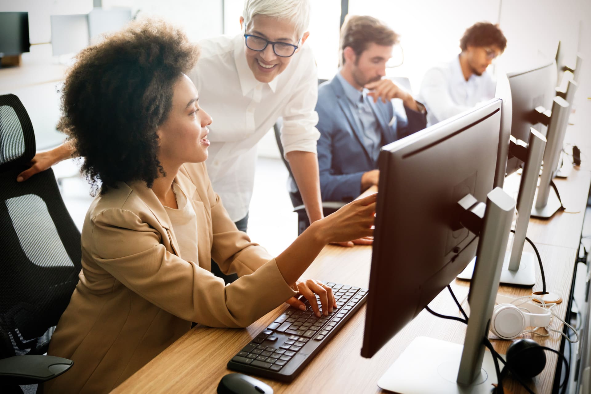 A group of colleagues works together in a modern office. One person sits at a desk using a computer with OCR software while another stands beside her, smiling. Two more coworkers work at computers in the background.